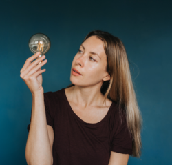 Woman looking curiously at a light bulb with blue background