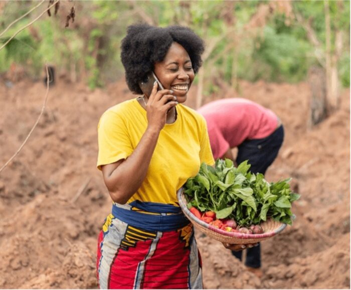 Woman laughing in field on the phone carrying a basket of farm produce